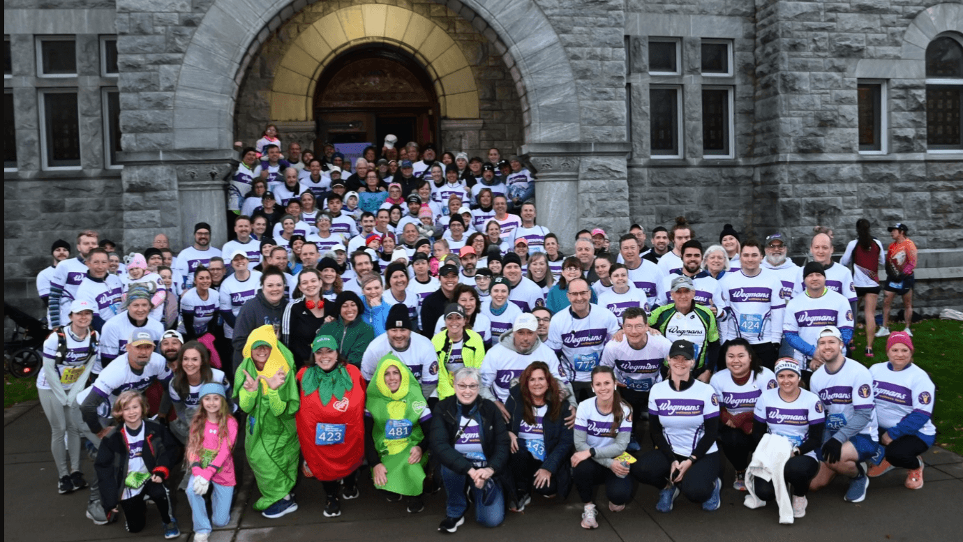 225 Wegmans employees in race shirts stand together and smile and steps of grey stone church